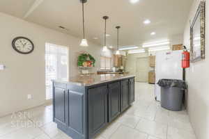 Kitchen featuring a kitchen island, light tile patterned flooring, recessed lighting, pendant lighting, and light stone countertops