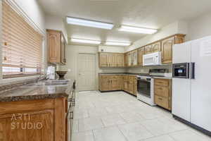 Kitchen featuring white appliances, dark countertops, light tile patterned flooring, a textured ceiling, and glass insert cabinets