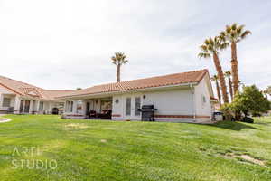 Back of property with a tile roof, a lawn, and stucco siding