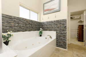 Bathroom featuring a tub with jets, a spacious closet, and stone finish flooring
