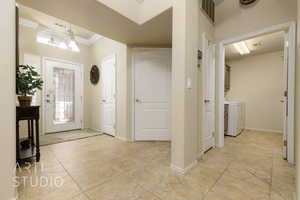 Foyer entrance with a chandelier, ornamental molding, independent washer and dryer, and light tile patterned flooring