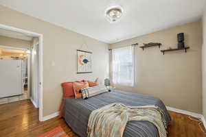 Bedroom featuring wood finished floors, freestanding refrigerator, a notable chandelier, and baseboards