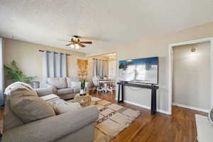 Living area featuring ceiling fan with notable chandelier, a textured ceiling, and dark wood-style floors