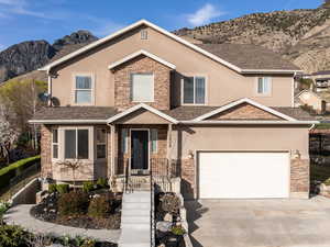 Traditional home featuring concrete driveway, stone siding, fence, and stucco siding
