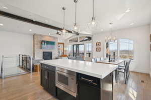 Kitchen with stainless steel microwave, dark cabinets, a large fireplace, light countertops, and light wood-style floors