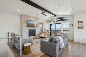 Living room with lofted ceiling with beams, a ceiling fan, wood finished floors, a tiled fireplace, and baseboards