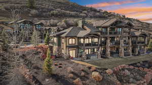 Rear view of property featuring a balcony, stucco siding, a chimney, stone siding, and a patio area