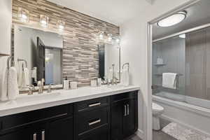 Bathroom with a sink, backsplash, toilet, and combined bath / shower with glass door