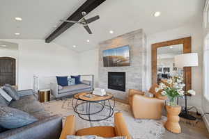 Living room featuring ceiling fan, wood finished floors, vaulted ceiling with beams, a tile fireplace, and baseboards
