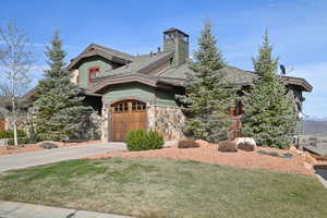 View of front of home featuring concrete driveway, a chimney, stone siding, a front lawn, and an attached garage