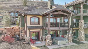 Back of house featuring cooling unit, metal roof, stone siding, a chimney, and a shingled roof