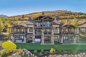 Back of house featuring a balcony, a chimney, stone siding, a patio area, and a hot tub