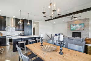 Dining space featuring lofted ceiling with beams, hardwood / wood-style flooring, a fireplace, recessed lighting, and ceiling fan with notable chandelier