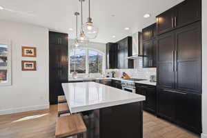 Kitchen featuring wall chimney exhaust hood, high end stainless steel range, a kitchen breakfast bar, light countertops, and decorative backsplash