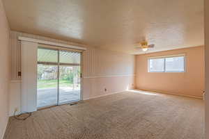 Carpeted empty room with a textured ceiling, ceiling fan, and visible vents