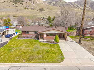 View of front facade with a mountain view, fence, brick siding, a front lawn, and driveway