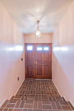 Entrance foyer featuring brick floor, baseboards, and a textured ceiling