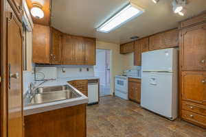 Kitchen with light countertops, brown cabinets, a sink, and white appliances