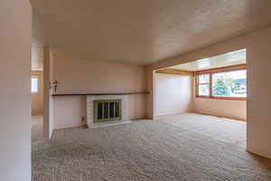 Unfurnished living room with carpet flooring, a brick fireplace, and a textured ceiling