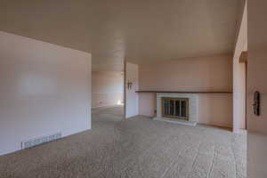 Unfurnished living room with a textured ceiling, a fireplace, visible vents, and carpet floors