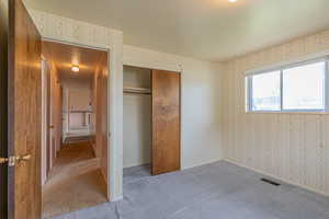 Unfurnished bedroom featuring wallpapered walls, a closet, visible vents, and carpet floors