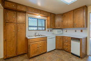 Kitchen featuring white appliances, light countertops, stone finish floor, brown cabinetry, and a sink