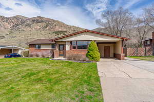 View of front of home with driveway, an attached carport, a front yard, brick siding, and fence