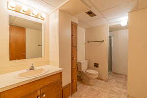 Bathroom featuring toilet, a paneled ceiling, a shower stall, and visible vents