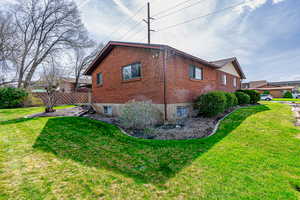View of side of property featuring a yard, fence, and brick siding