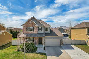 View of front of property featuring an attached garage, concrete driveway, stone siding, and a gate