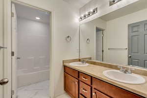 Full bathroom featuring bathing tub / shower combination, double vanity, marble finish floor, and a sink