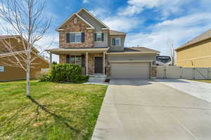 Craftsman-style house with stucco siding, driveway, stone siding, a front lawn, and a gate