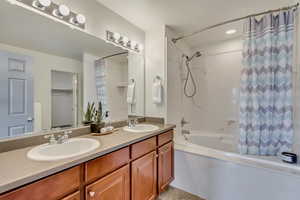 Bathroom with shower / bathtub combination with curtain, double vanity, and a sink