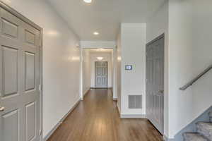 Corridor with hardwood / wood-style floors, baseboards, visible vents, and stairway