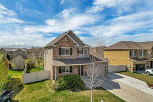 View of front of home with a front yard, driveway, stone siding, and fence