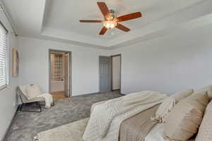Bedroom with baseboards, ensuite bath, a ceiling fan, carpet floors, and a raised ceiling