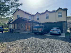 View of front facade featuring driveway, a garage, stone siding, and stucco siding