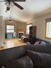 Living room featuring a ceiling fan, wood finished floors, a fireplace, and lofted ceiling