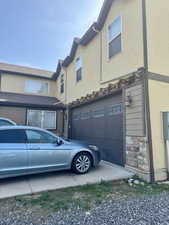View of side of property with a garage, stucco siding, and stone siding