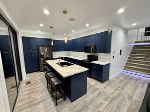 Kitchen featuring a kitchen bar, light wood-type flooring, black appliances, blue cabinets, and a sink