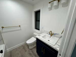 Bathroom featuring toilet, vanity, wood finished floors, and baseboards