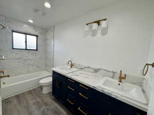 Full bath with toilet, wood finished floors, double vanity, and a sink