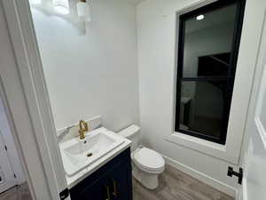 Half bath with vanity, toilet, and wood finished floors