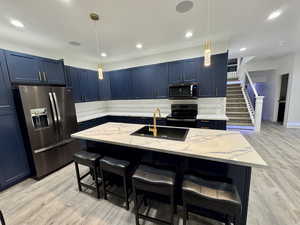 Kitchen with stainless steel appliances, a sink, blue cabinetry, and light stone counters