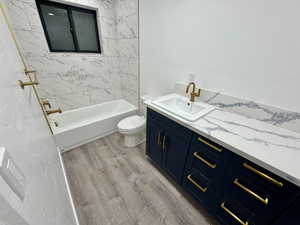 Bathroom featuring toilet, wood finished floors, vanity, and  shower combination