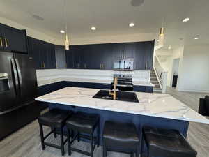Kitchen with black fridge with ice dispenser, a sink, stainless steel range with electric cooktop, light stone countertops, and decorative backsplash