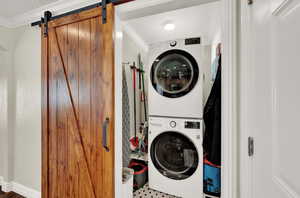 Laundry room featuring a barn door, stacked washer / drying machine, crown molding, and laundry area