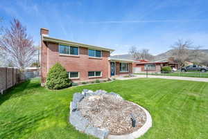 View of front of home with a front yard, brick siding, a fenced backyard, and a chimney