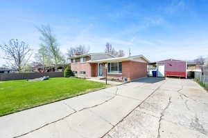 Tri-level home featuring a front yard, fence, brick siding, a chimney, and driveway