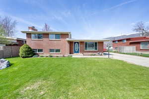 Tri-level home featuring a front yard, fence, brick siding, a chimney, and driveway